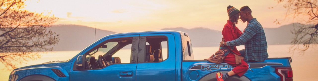 A couple hugging and sitting in the bed of a blue Ford truck