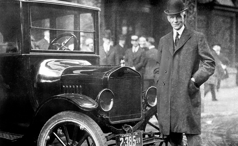 Black and white photo of Henry Ford standing next to a vehicle