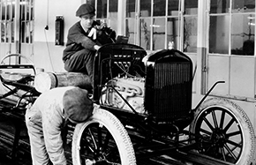 Black and white photo of two men working on a car assembly line