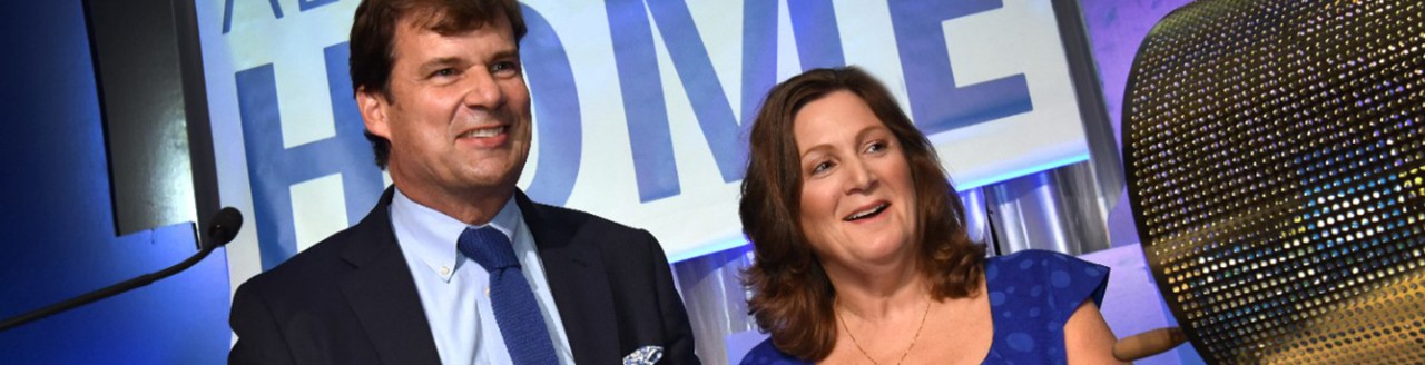 Jim Farley and Elena Ford smiling and clapping at a podium