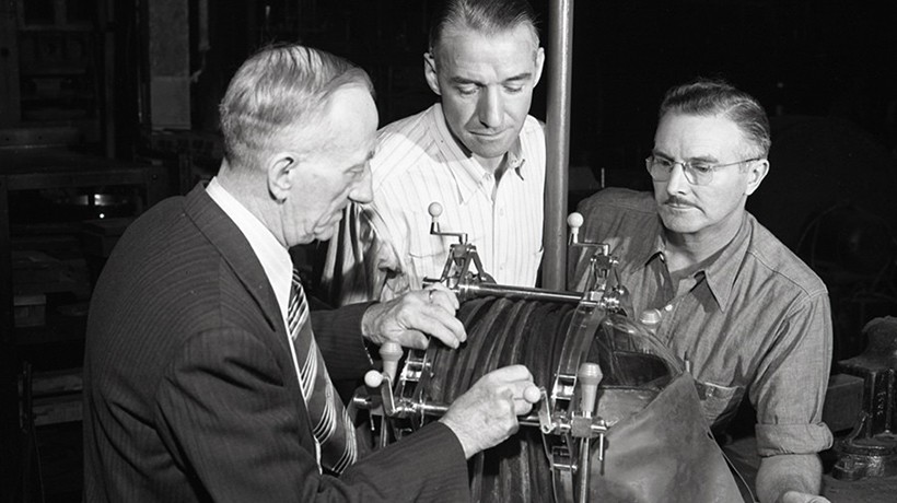 Black and white image of 3 men with an iron lung