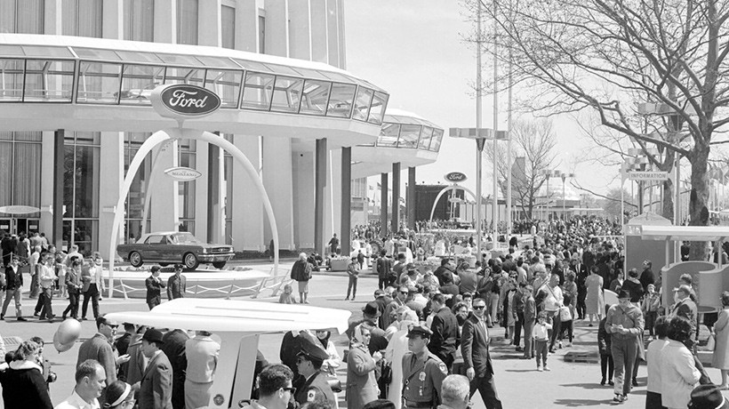 A black and white photo of many crowds standing outside a large building