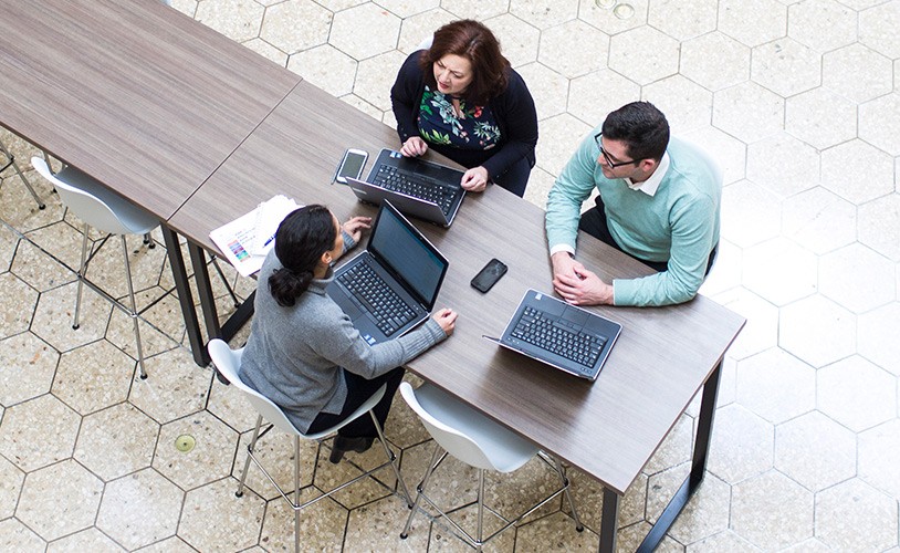 Three people working with laptops in cafeteria