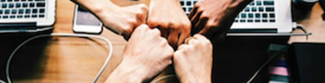 Image of five fists held against each other over laptop computers