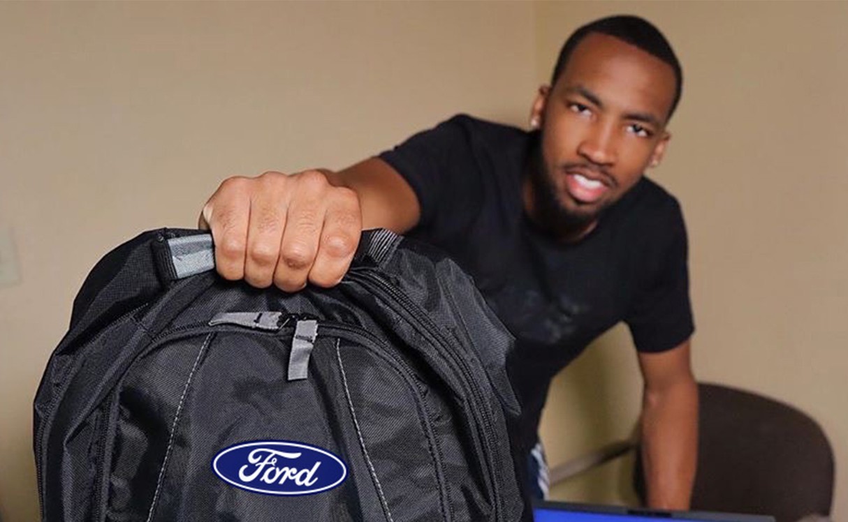 A male intern holding a Ford backpack and smiling