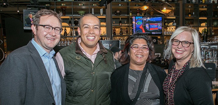 two men and two women arm in arm at a social gathering smiling for camera