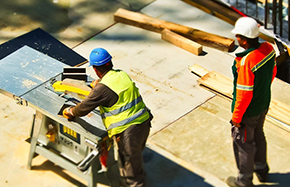 two construction workings working on roof with table saw and wood
