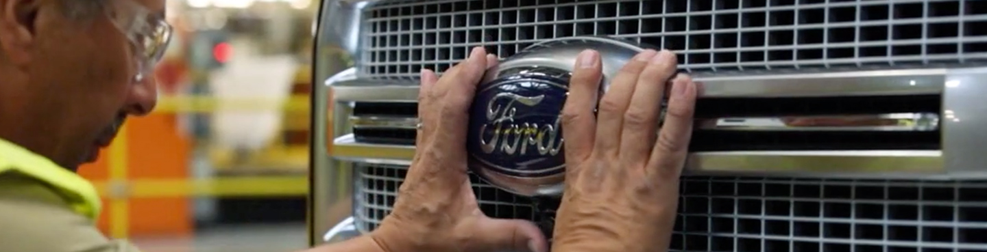man touching front grill and Ford logo