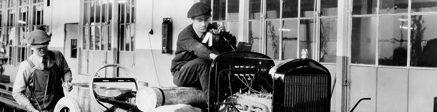 Black and white photo of two men working on a car assembly line