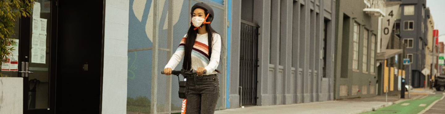 A woman riding a Spin escooter through a downtown area