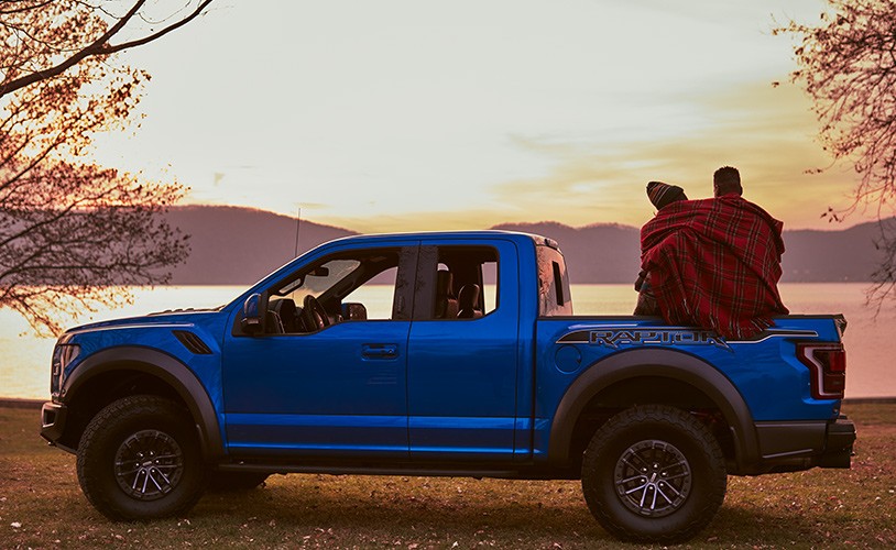 Two people wrapped in blanket in bed of F150 looking at sunset