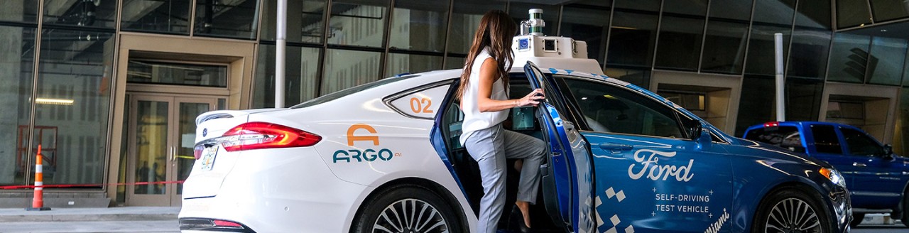 A woman getting into the backseat of a Ford branded autonomous vehicle