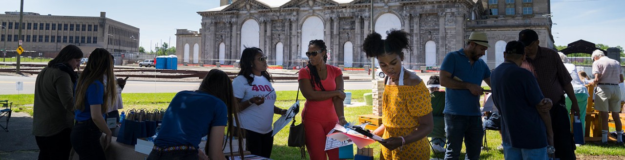 A group of people at an information booth outside of the Michigan Central Station building