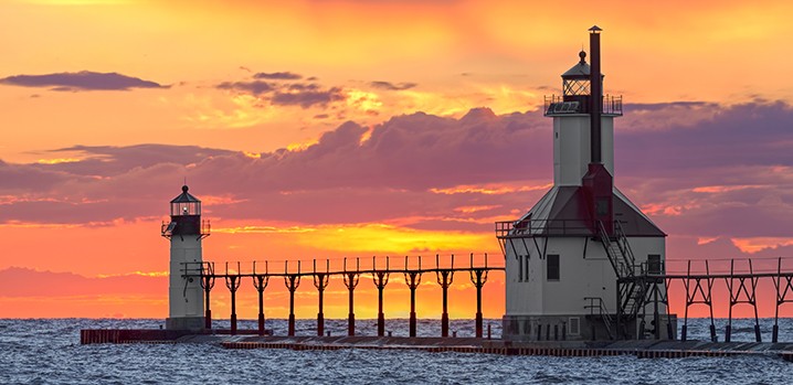 A boardwalk connecting two lighthouses with a sunset in the background