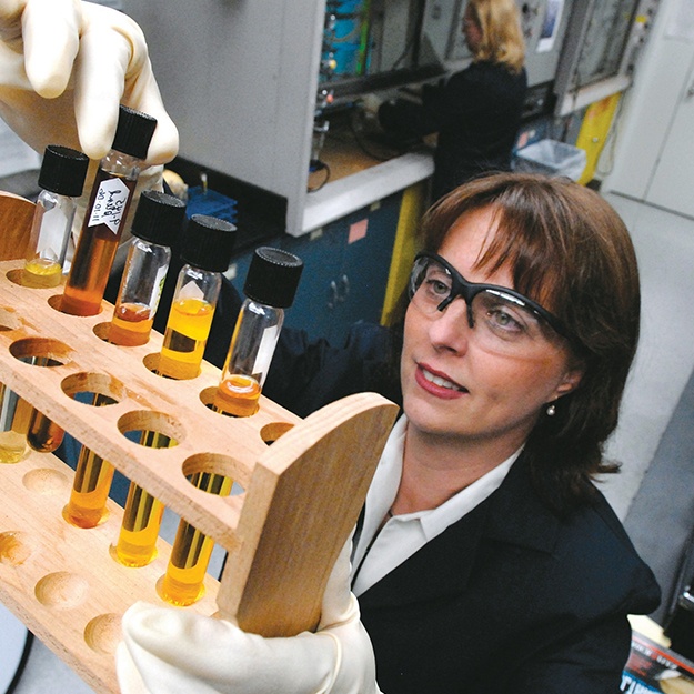 A woman with safety glasses looking at test tubes