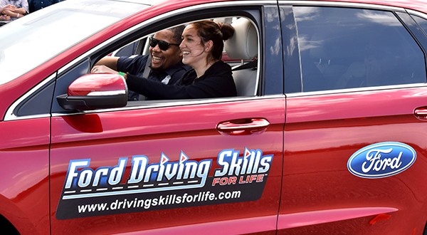 A Ford Driving Skills for Life red vehicle with two people inside