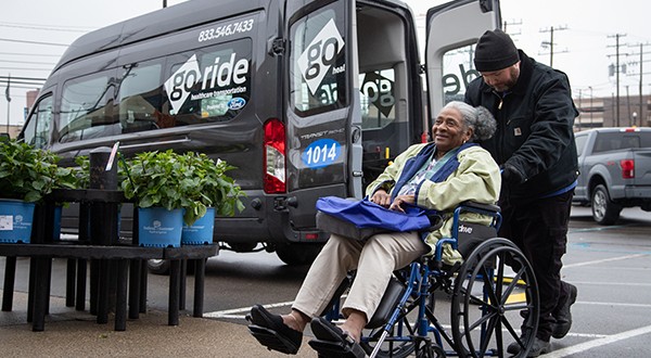 A man pushing a woman sitting in a wheelchair with a go-ride van behind them