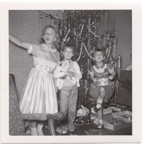 Image of three excited children with their toys in front of the christmas tree.