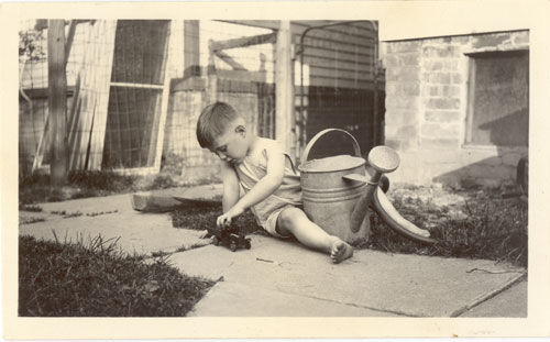 Image of a boy playing outside with a watering can and a toy truck.