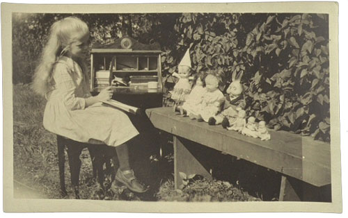 Image of a little girl outside playing school with her dolls.