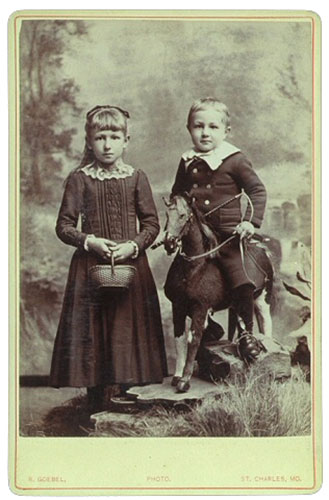 Image of girl standing with a basket and a boy on a toy horse.